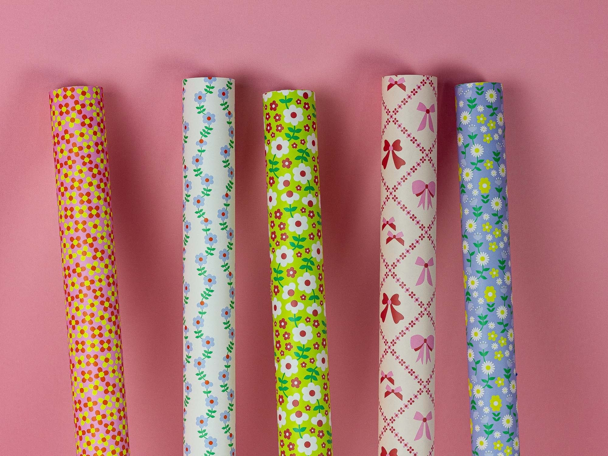 a group of different colored wrapping paper on a pink surface
