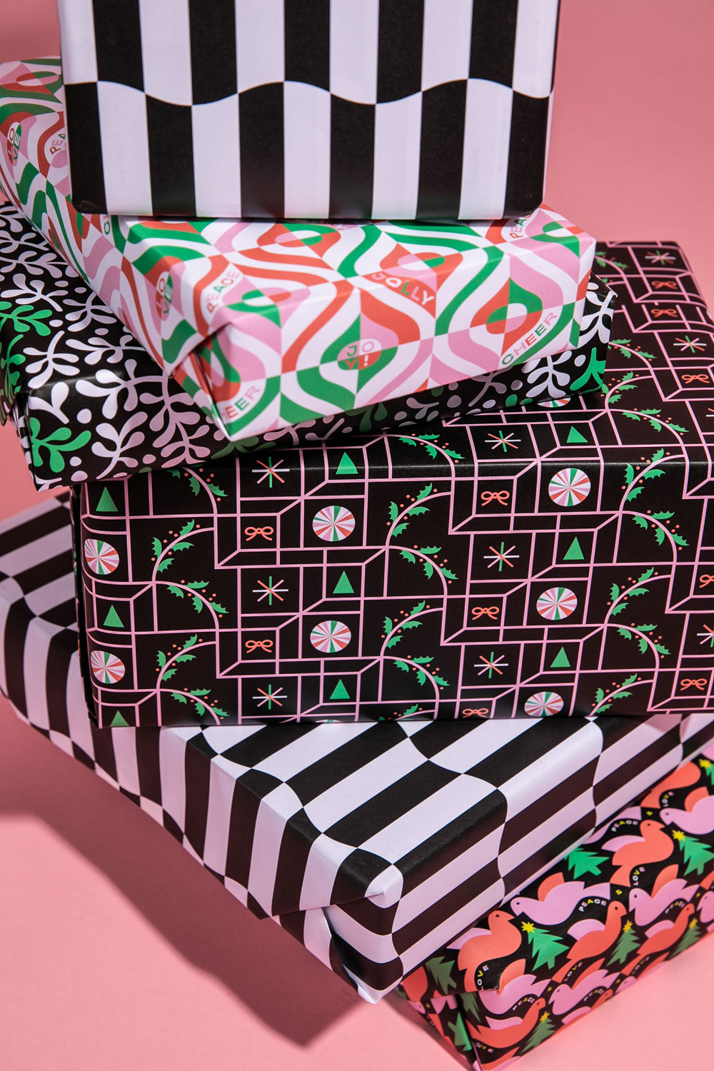 Stack of presents wrapped in mid-century inspired Christmas wrapping paper with abstract patterns and holiday illustrations.